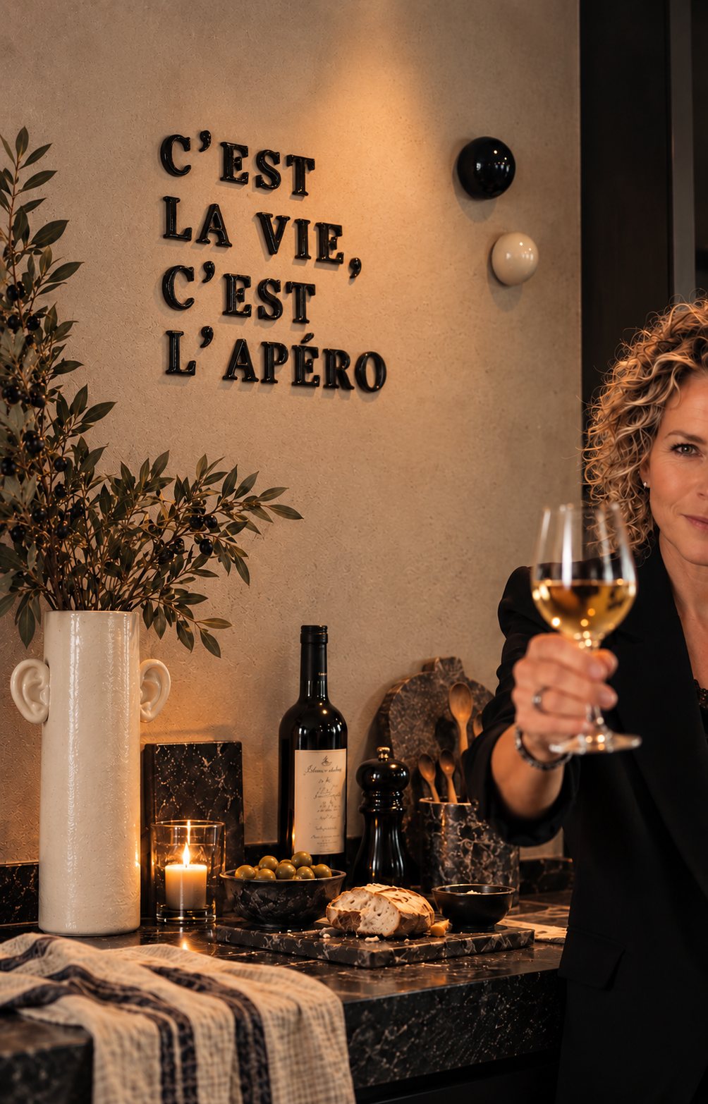 Sfeerbeeld van KeraIEK: keramische letters C’EST LA VIE, C’EST L’APÉRO aan de muur, keramiek op aanrecht en de maker met wijnglas