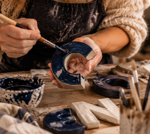 Een keramische letter wordt met een kwast blauw geglazuurd tijdens de workshop Grote Woorden